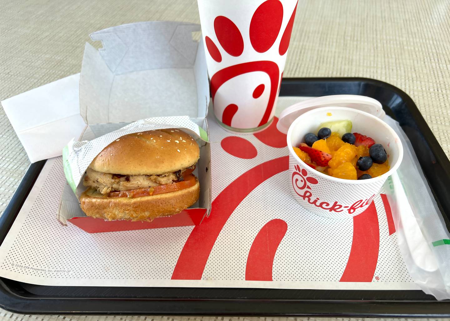 Close up on Grilled Chicken Sandwich and fruit cup with soda cup in background on a serving tray at Chick-fil-a fast food restaurant.